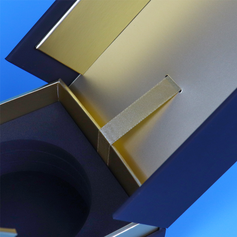 Close-up of a blue and gold magnetic box with a fabric pull tab attached to the inner flap, highlighting the hinge and closure mechanism.