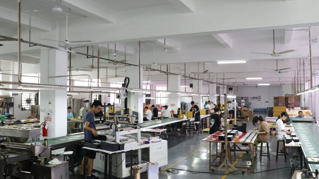Factory floor with workers assembling boxes on production lines, emphasizing the importance of consistent manufacturing processes for reliable child-resistant packaging.