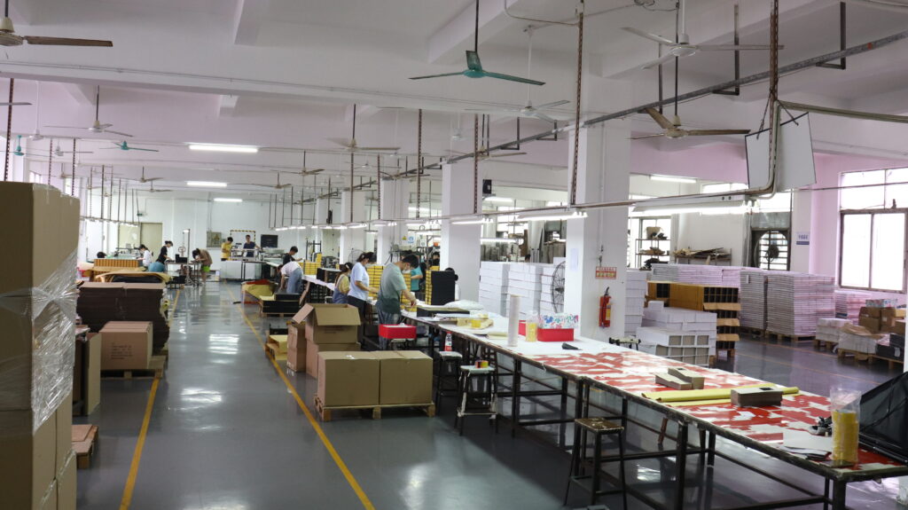 Large-scale packaging factory with workers assembling boxes on production lines, highlighting the importance of consistent manufacturing processes for child-resistant vape packaging compliance.