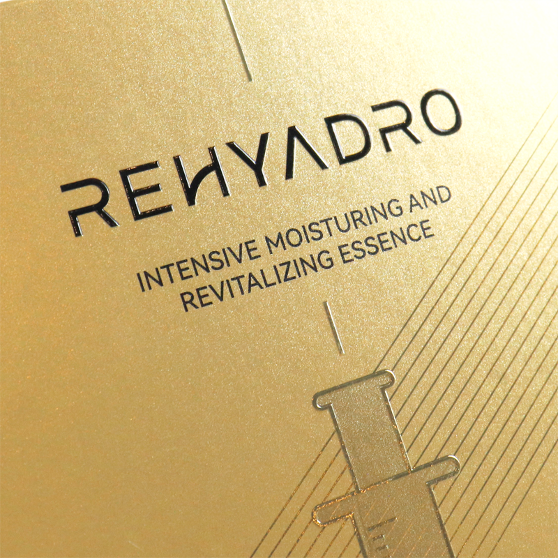 Close-up of a gold metallic surface with debossed text "REHYDRO" and a syringe graphic, featuring fine lines and clean typography.