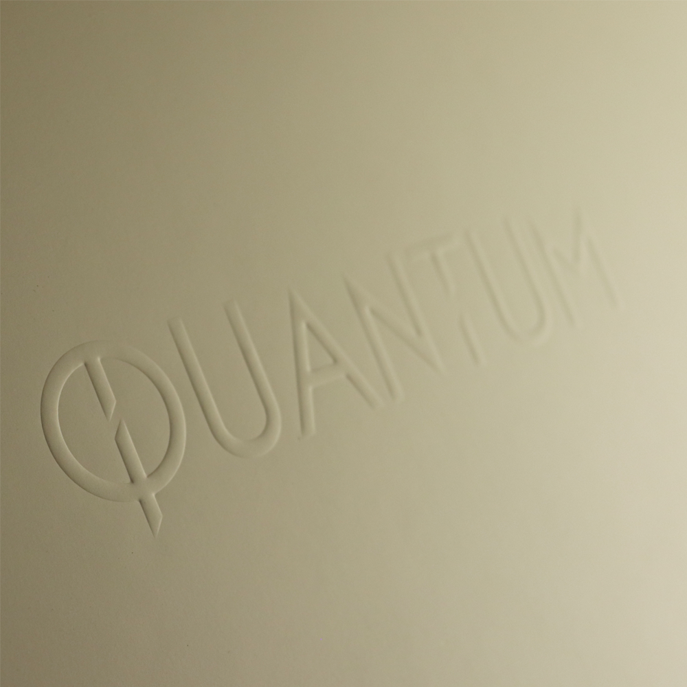 Close-up of white embossed "QUANTUM" logo on a matte surface, featuring subtle depth and refined typography.
