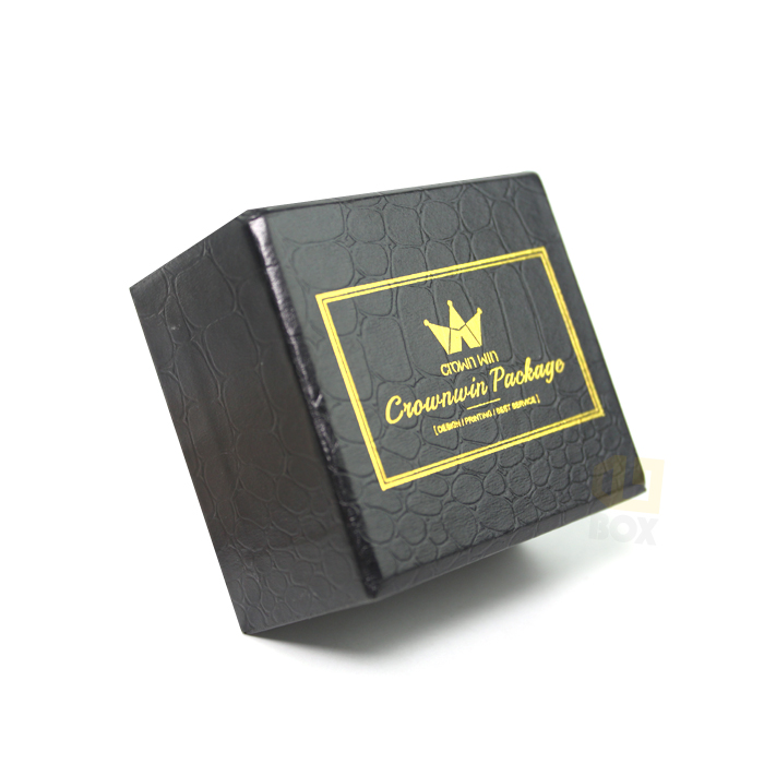 Black rigid box with crocodile-like embossed texture and gold foil-stamped logo inside a rectangular border, showcasing high-end finishes.