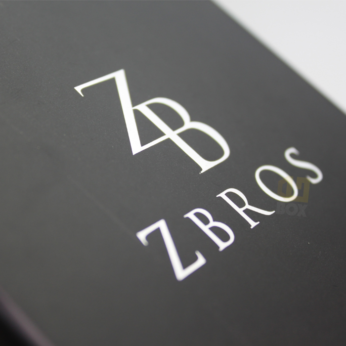 White foil-stamped "ZBROS" logo on a black matte background, highlighting crisp typography and reflective contrast.