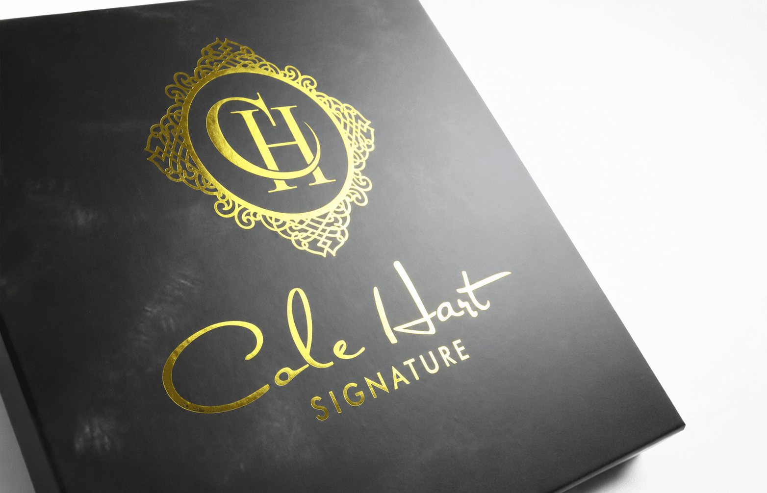 Close-up of a custom black rigid gift packaging box with an elegant gold foil logo and decorative branding for premium luxury products.