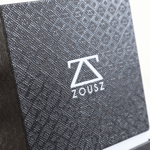A macro close-up of a custom geometric embossed grid texture pattern on dark grey cardstock with a crisp white printed ZOUSZ logo.