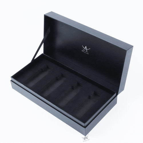 An open custom-printed black neck-style cardboard box featuring a black satin ribbon lid stay and a precision die-cut velvet packaging tray with 4 compartments.