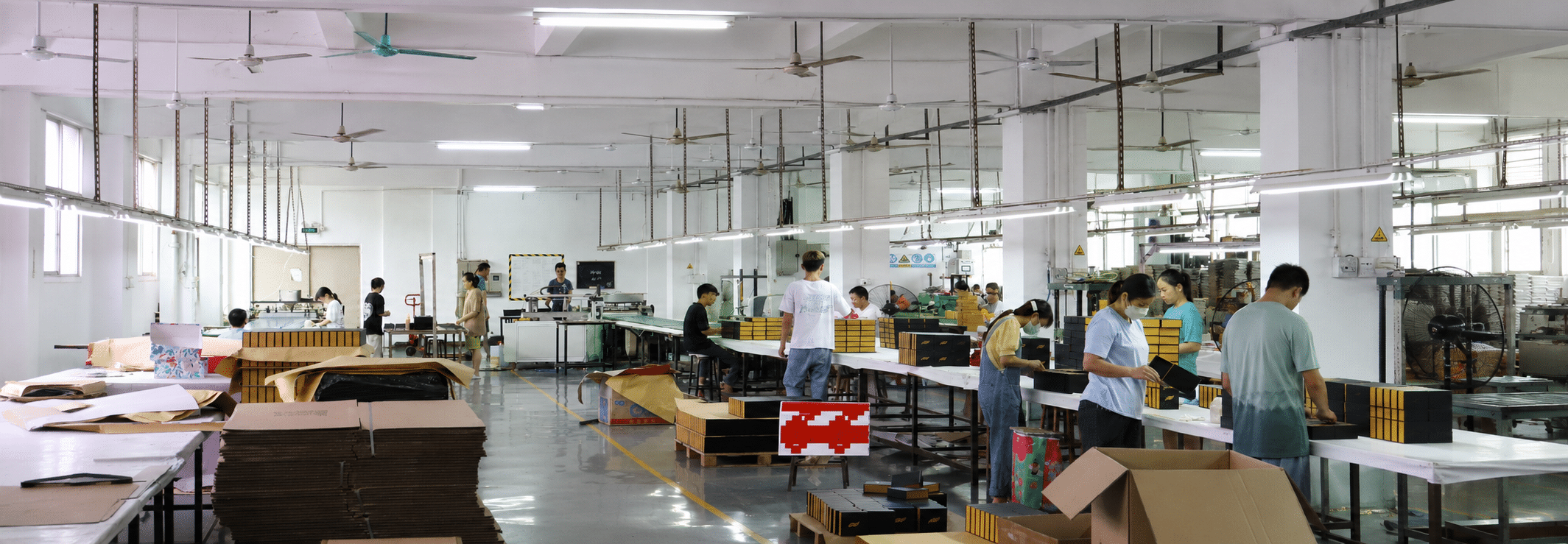 Workers assembling custom rigid gift boxes on a paper packaging factory production line for wholesale and branded packaging orders.