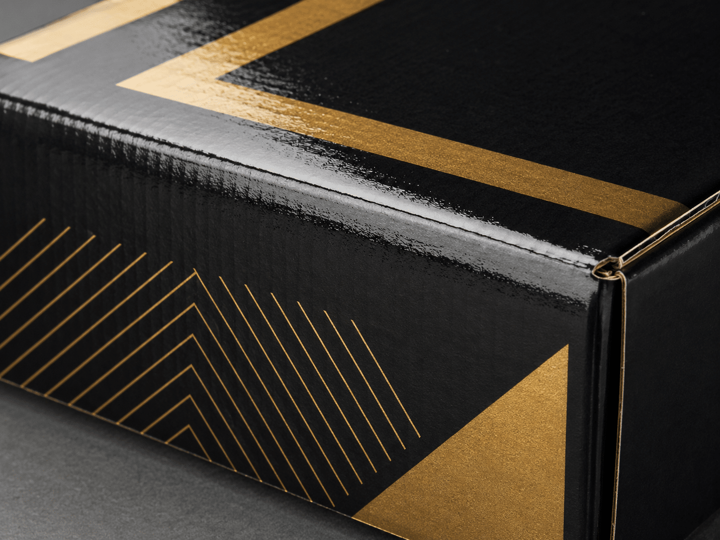 Close-up of a custom black corrugated packaging box with glossy lamination, gold foil geometric printing and reinforced folded edges