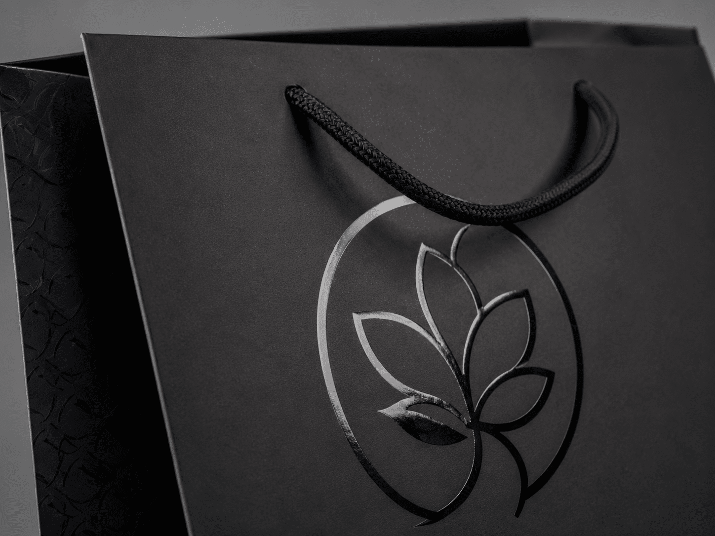 Close-up of a custom black paper shopping bag with braided rope handles, glossy spot UV logo and textured side printing