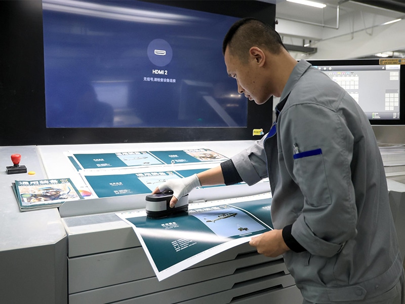 Packaging technician inspecting printed paper sheets during custom paper bag production to ensure accurate color and print quality
