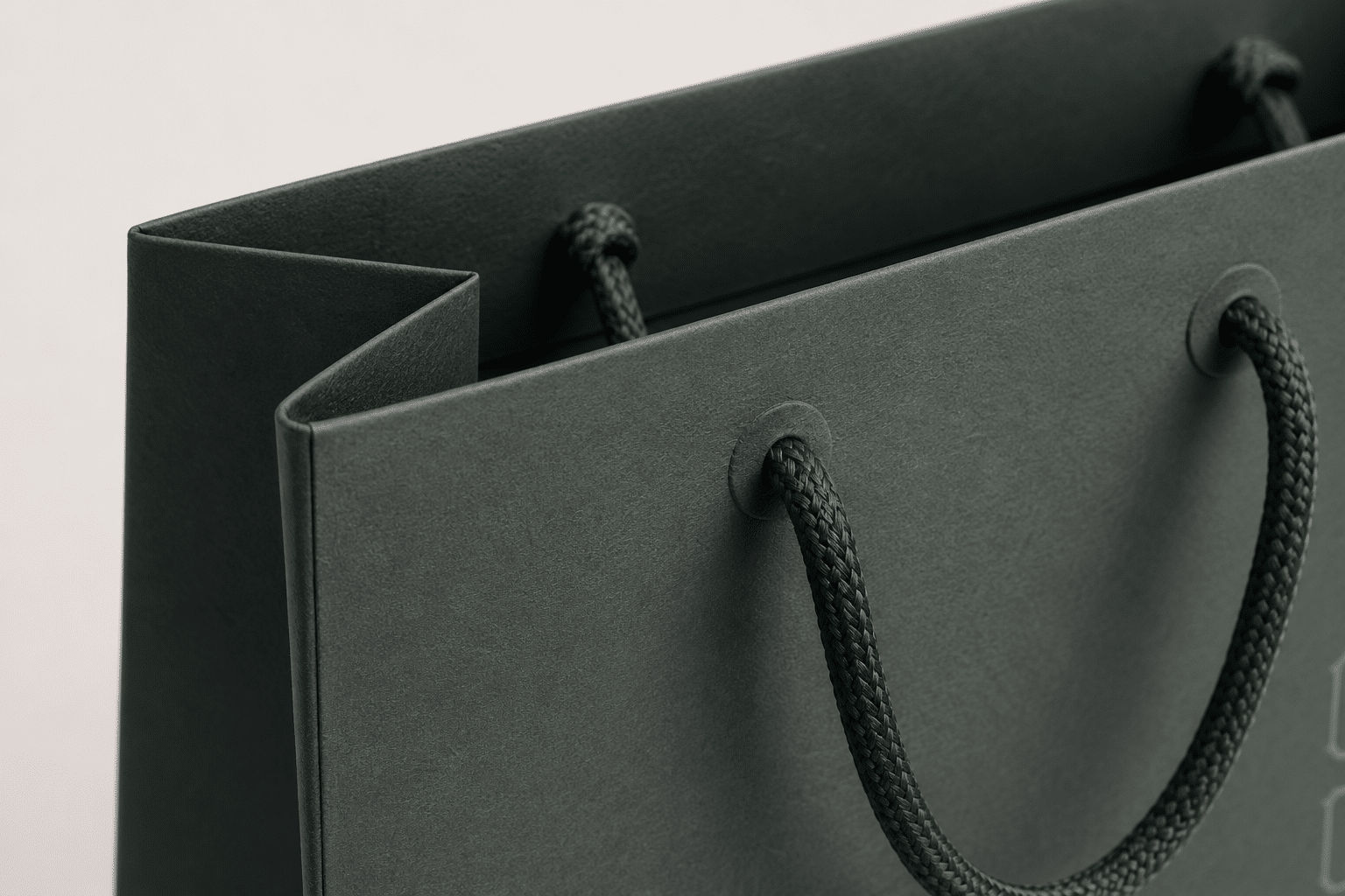 Close-up of a custom dark green paper shopping bag with reinforced handle holes and matching braided rope handles