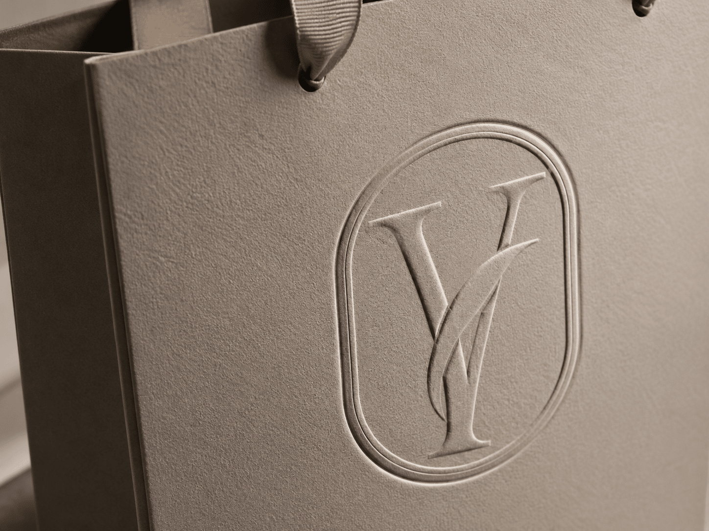 Close-up of a custom beige textured paper shopping bag with ribbon handles and raised embossed monogram logo
