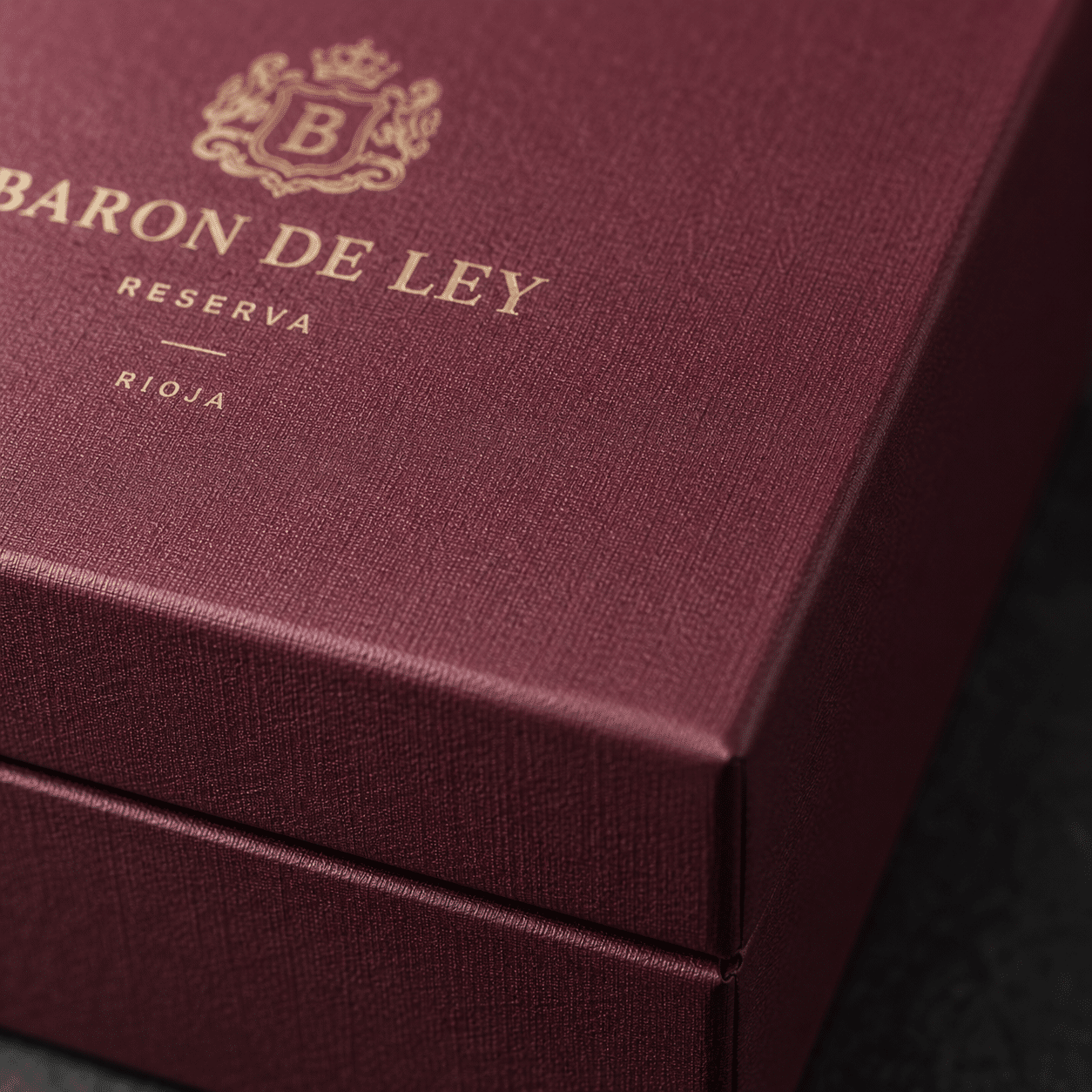 Close-up of a burgundy custom wine gift box made with textured paper and finished with an elegant gold foil logo