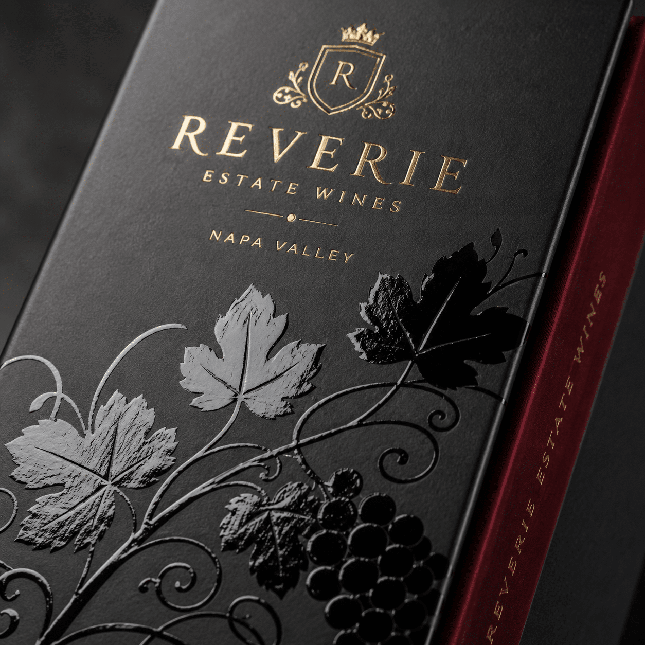 Close-up of a custom black wine packaging box with gold foil branding, glossy spot UV grape leaves and a burgundy inner tray