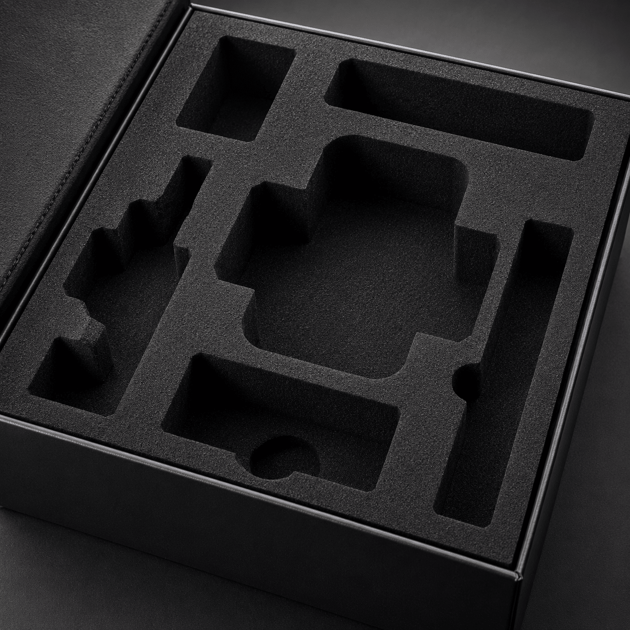 Black rigid packaging box with a custom-cut EVA foam insert featuring multiple protective compartments for different products and accessories.