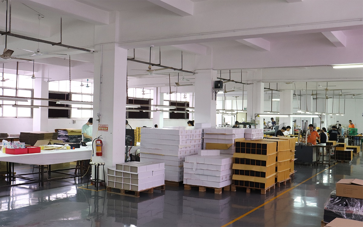 Custom packaging insert factory workshop with workers assembling and inspecting paper boxes, foam inserts and protective packaging components.
