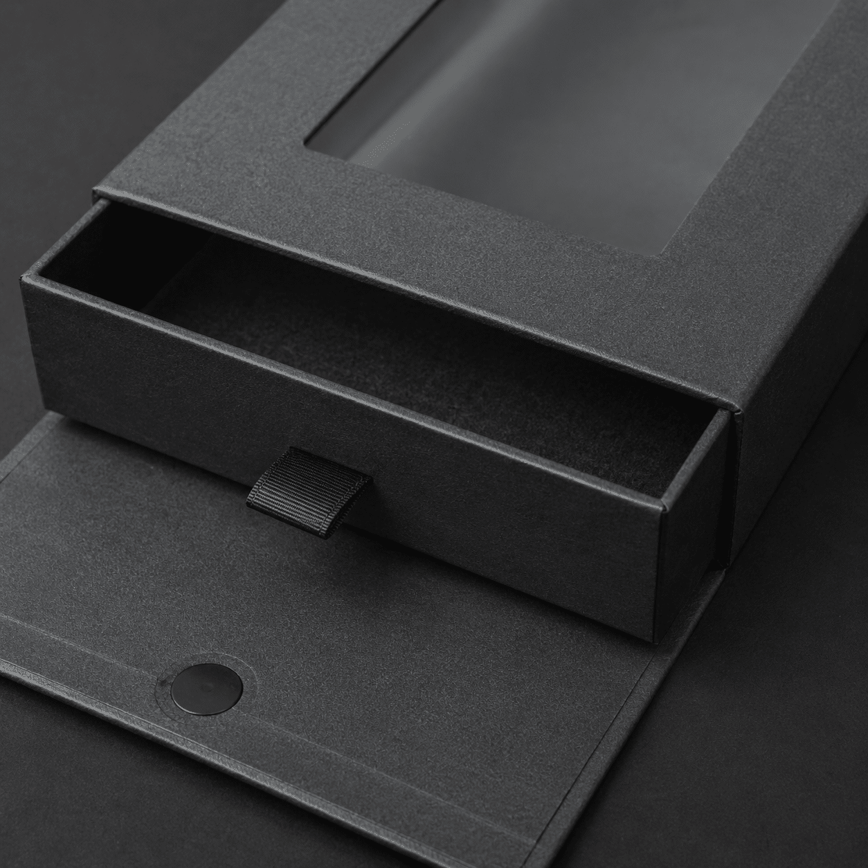 Close-up of a black rigid drawer box with ribbon pull tab, window sleeve and magnetic closure detail