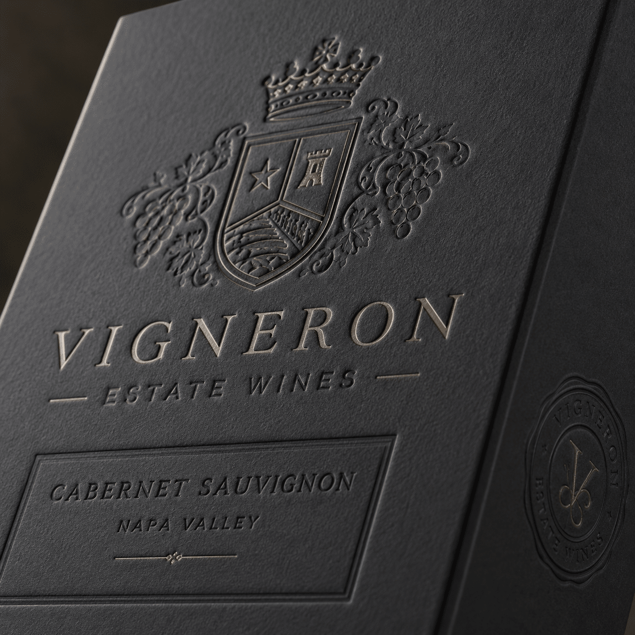 Close-up of a luxury black wine packaging box featuring an embossed crest, grape motifs and selective gold foil details