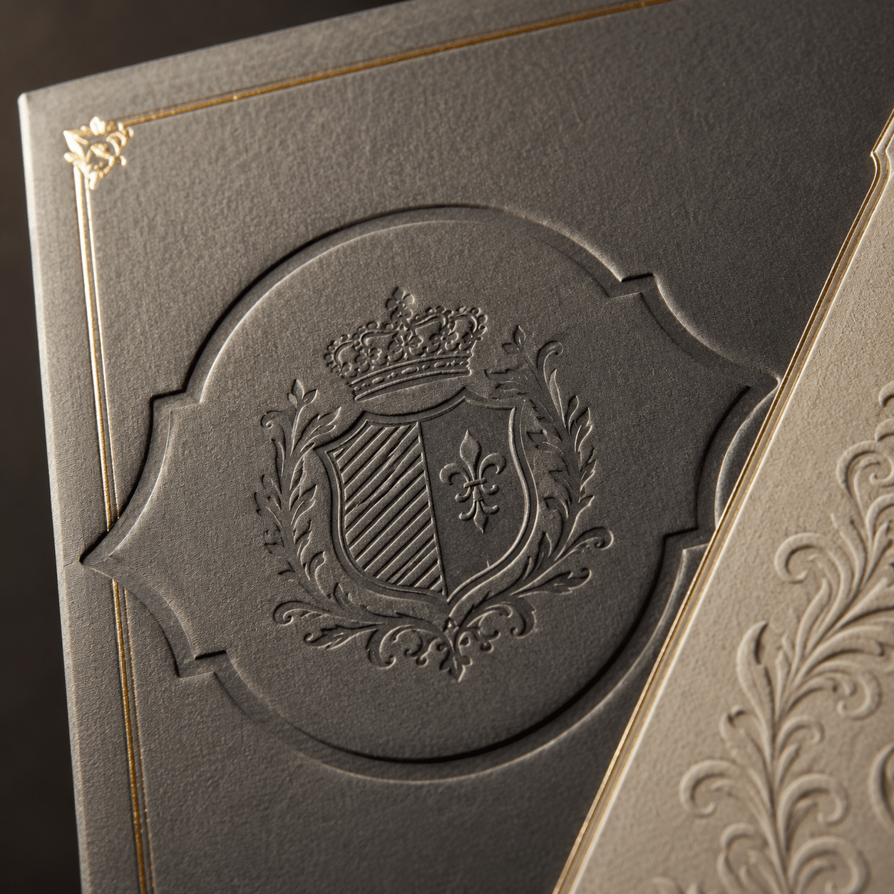 Close-up of an embossed crest and gold foil border on textured luxury rigid box packaging.