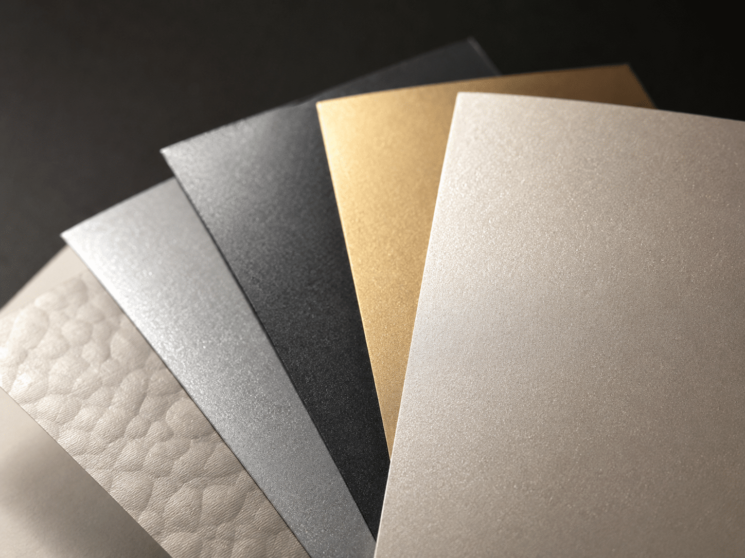 Selection of gold, silver, black and pearl textured specialty papers for luxury custom packaging box production.
