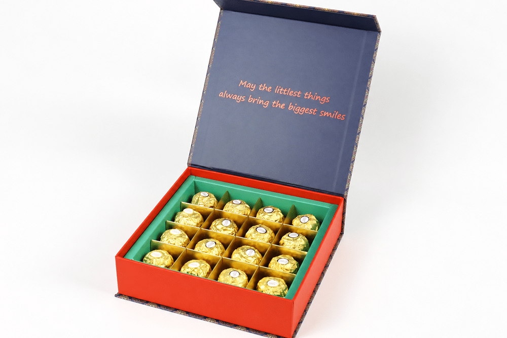 Open red chocolate gift box with green dividers holding individually wrapped chocolates